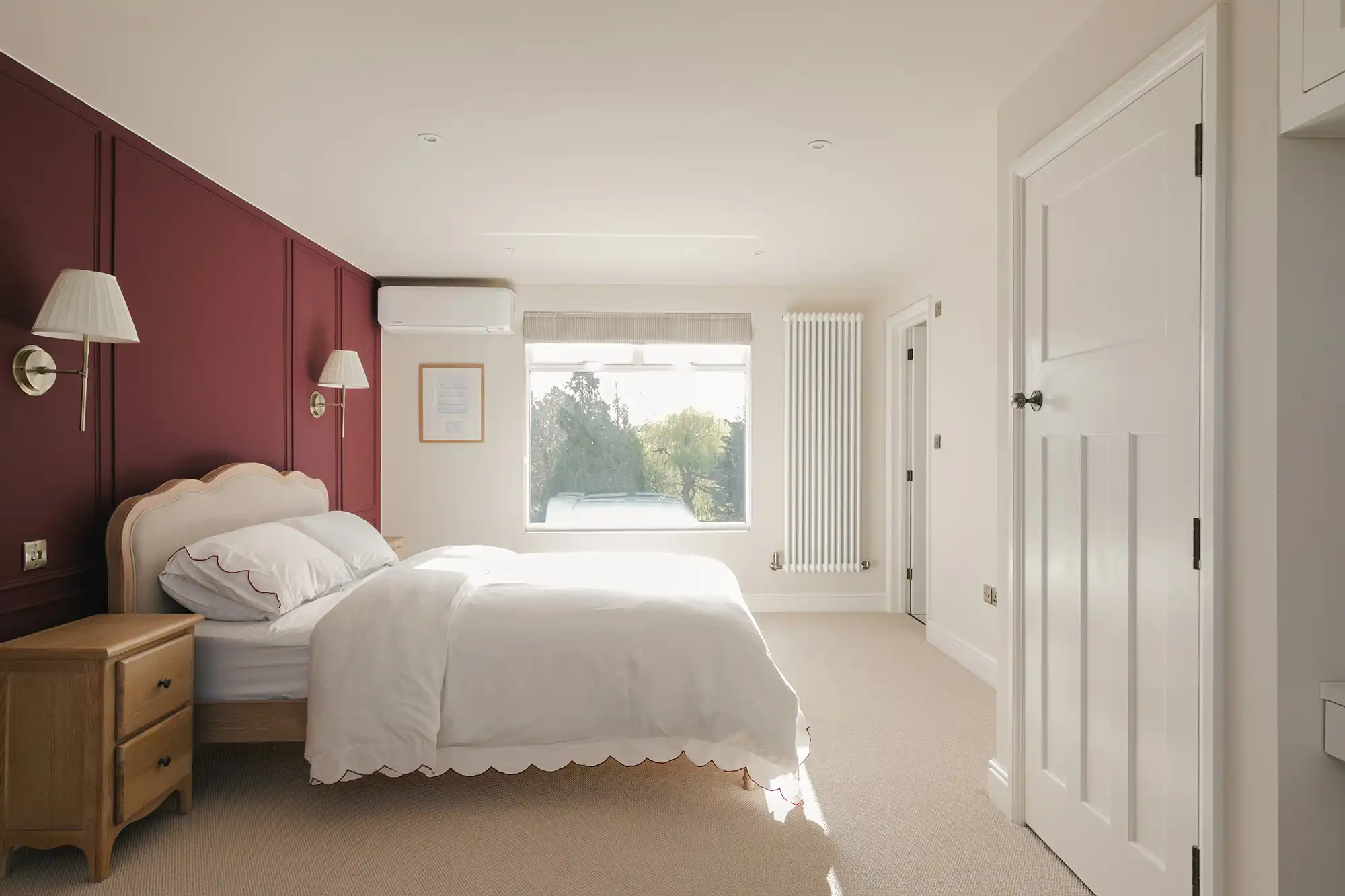 Bright and modern bedroom featuring a bed, nightstand, and large window. Walls are accented in dark red, creating a cozy ambiance.